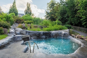 Área de águas termais com piscina, rodeada por rochas e vegetação.