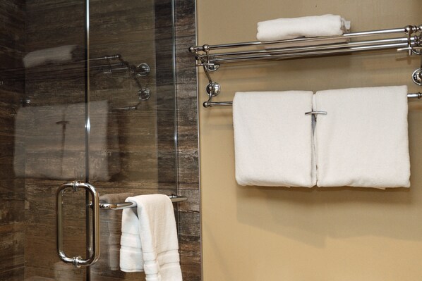 A bathroom with a glass shower enclosure, a towel rack with two towels, and a beige wall.