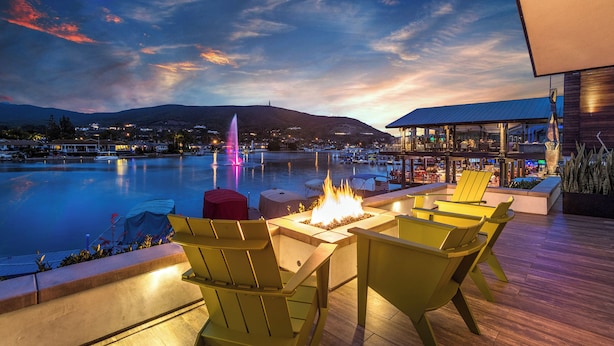 An outdoor seating area with chairs and a fire feature, overlooking a body of water and a distant mountain range.