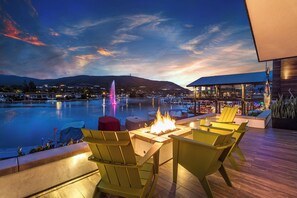 An outdoor seating area with chairs and a fire feature, overlooking a body of water and a distant mountain range.