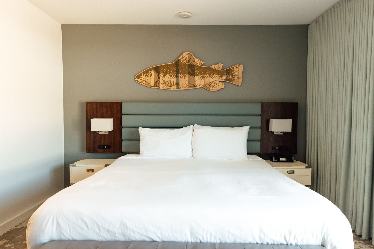 A hotel room with a large bed, two bedside tables, a wall-mounted fish decoration, and a headboard with a light green panel.