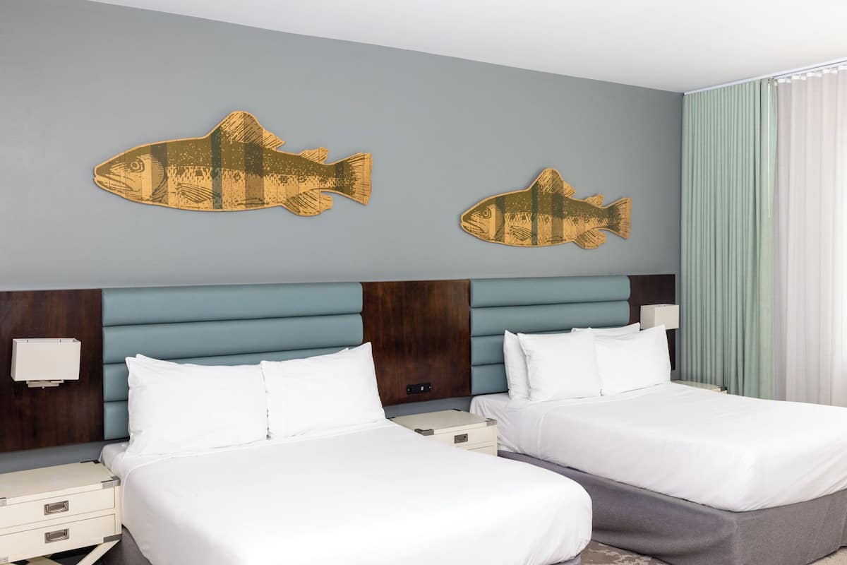 Een hotelkamer met twee bedden, een houten hoofdbord en twee visdecoraties aan de muur.