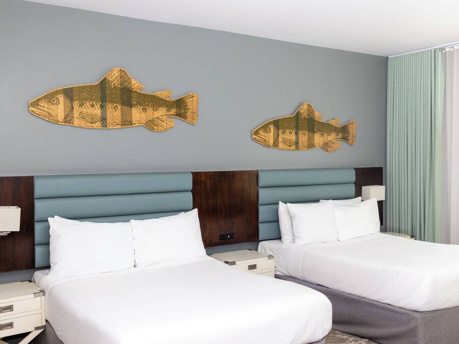 A hotel room with two beds, a wooden headboard, and two wall-mounted fish decorations.