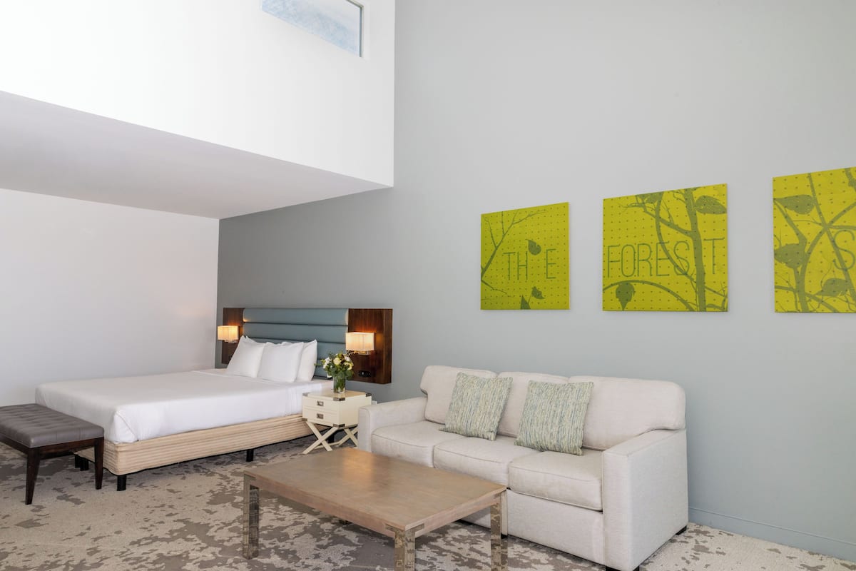 Een moderne hotelkamer met een bed, een bank, een bijzettafeltje en drie gele kunstwerken aan de muur.