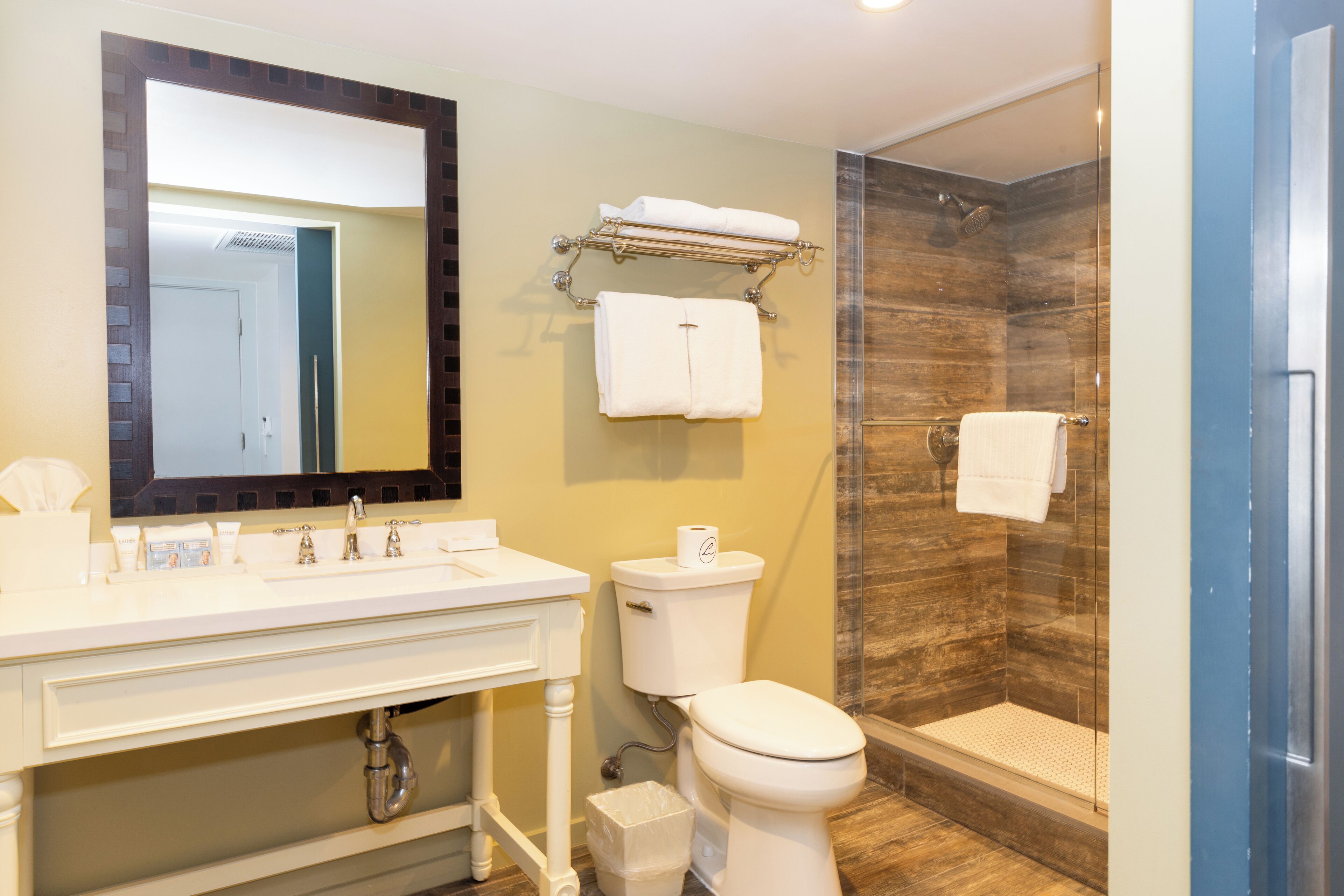 A modern bathroom with a white sink, mirror, and toilet, a glass shower enclosure, and a towel rack with towels.