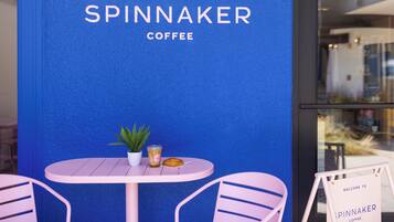 Pared azul con el texto "SPINNAKER COFFEE" y una pequeña mesa con una planta en maceta, un vaso y un pastel.