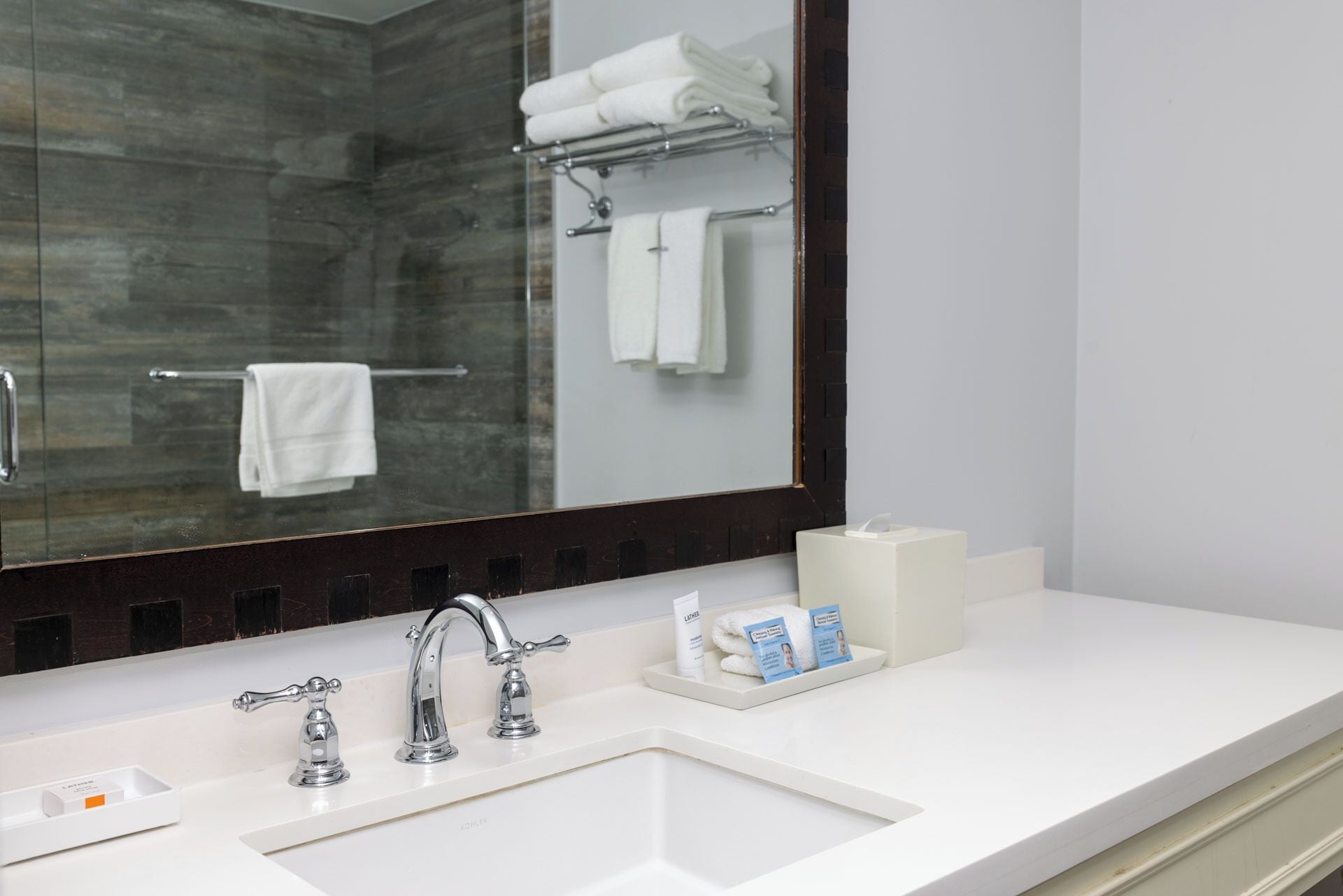 A bathroom with a white sink, two faucets, a mirror, and a towel rack with folded towels.