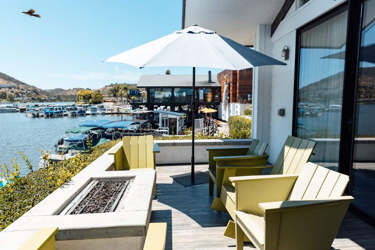 Een terras met buitenmeubilair, een vuurkorf en uitzicht op een jachthaven en heuvels.