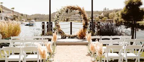 A wedding aisle with white chairs and floral decorations leading to a decorated arch.