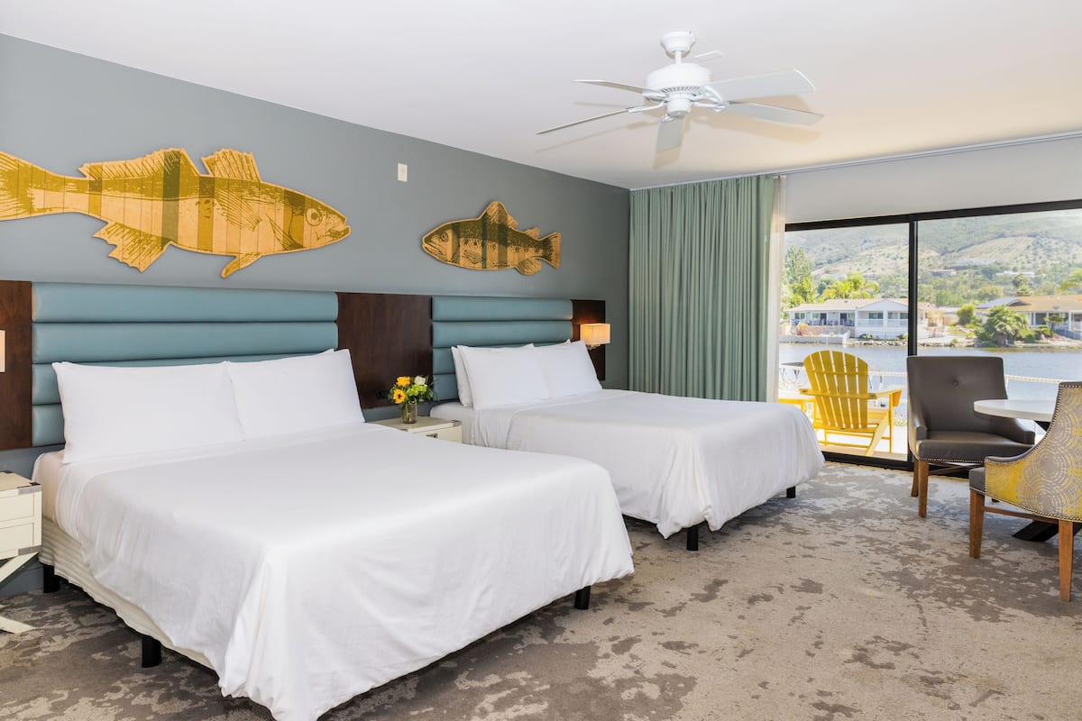Een hotelkamer met twee bedden, een plafondventilator, een groot raam met uitzicht op de omgeving en een stoel bij het raam.