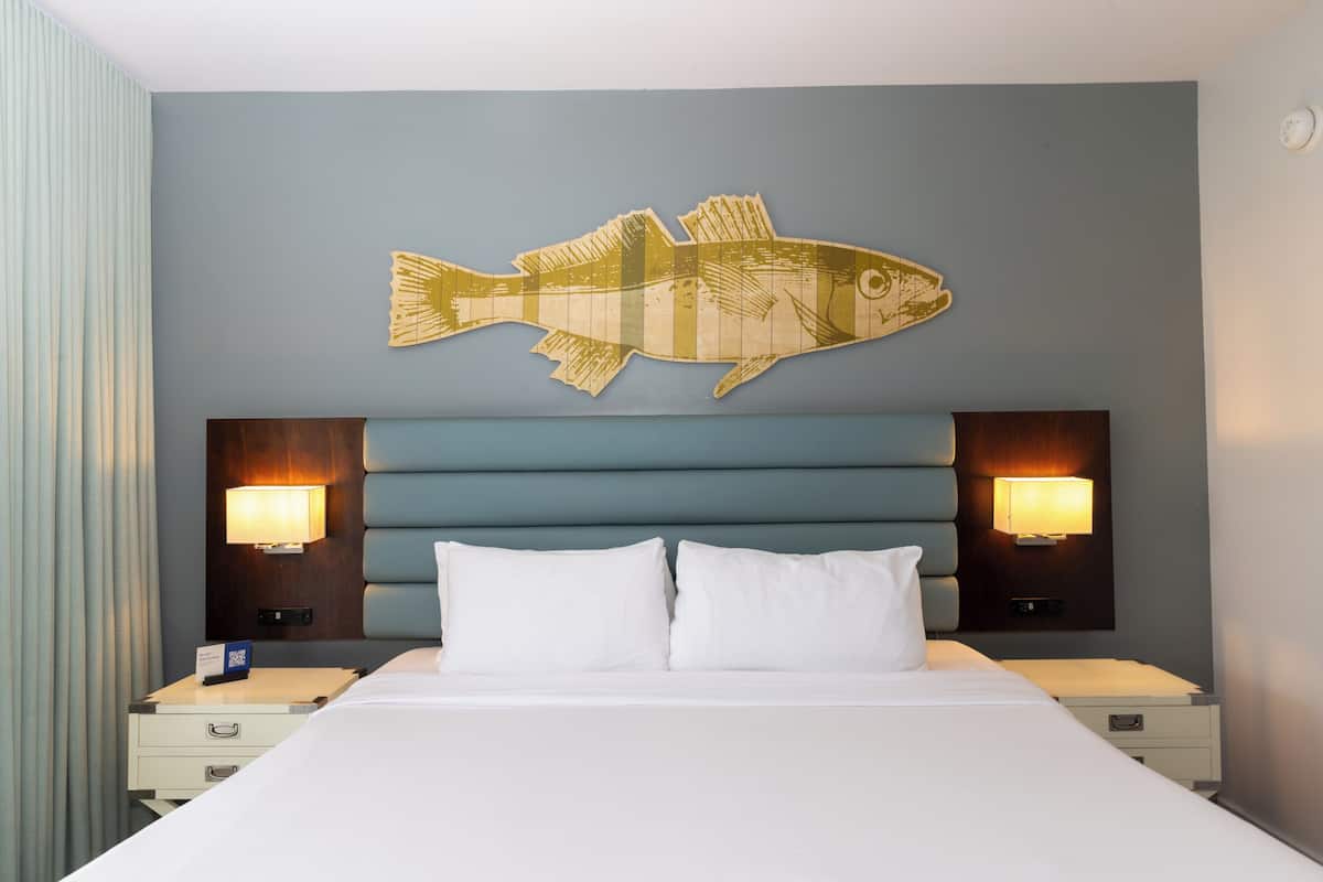 Een hotelkamer met een bed, twee nachtkastjes, een viskunstwerk aan de wand en twee wandlampen.