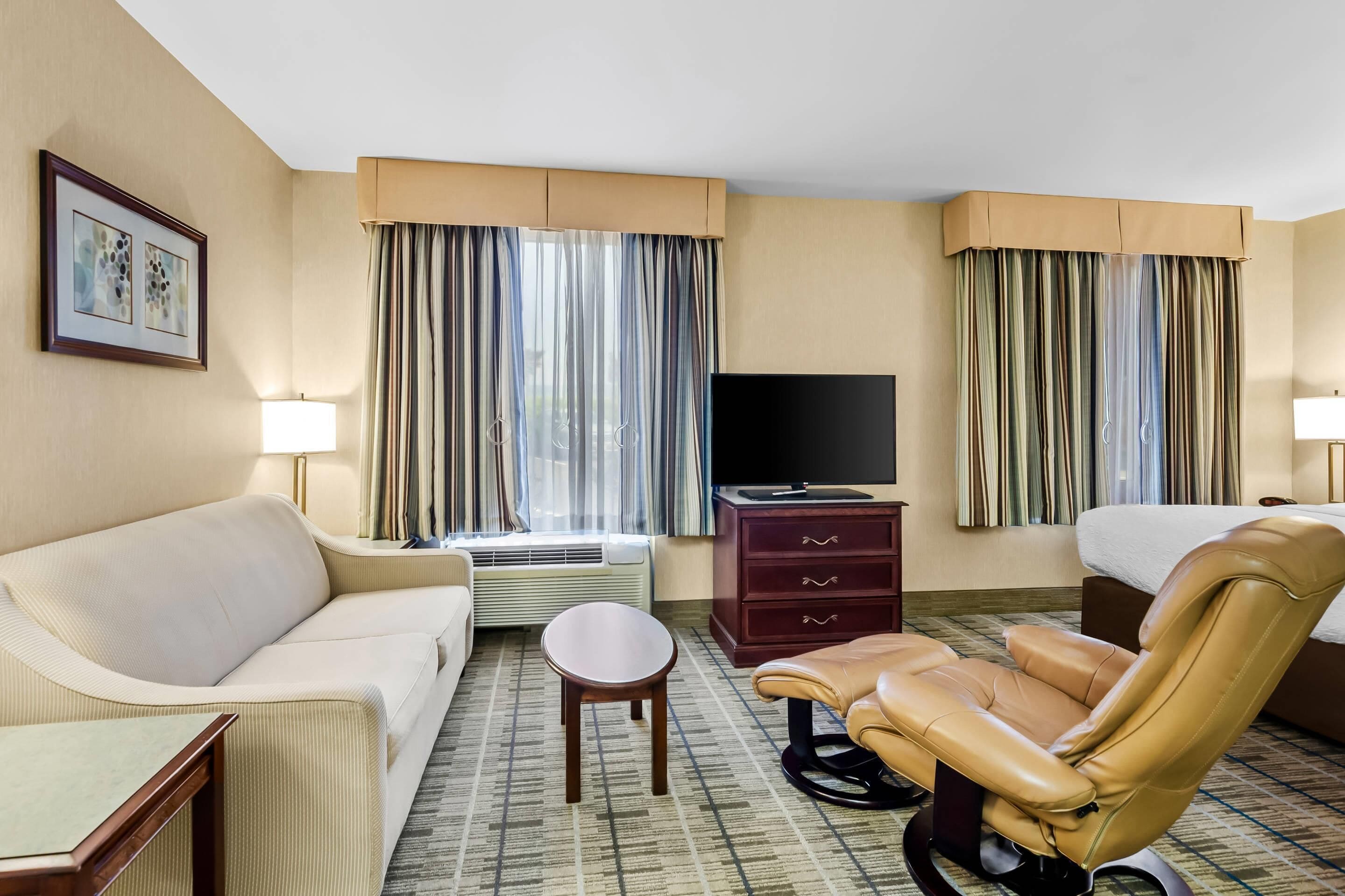 A hotel room with a sofa, a chair, a TV, a desk, and a bed.