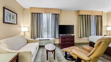 Una habitación de hotel con sofá, una silla, televisión, escritorio y cama.