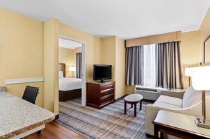 Una habitación de hotel con cama, televisor, sofá, una mesita y ventana con cortinas.