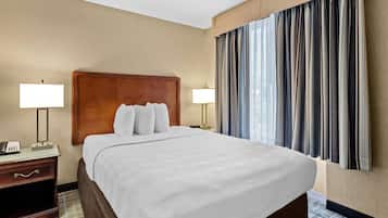 Habitación de hotel con una cama grande, dos lámparas de noche, cabecera de madera y vistas a la ciudad a través de cortinas.