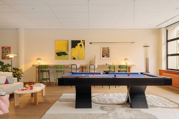 A pool table in a room with a sofa, chairs, and artwork on the walls.