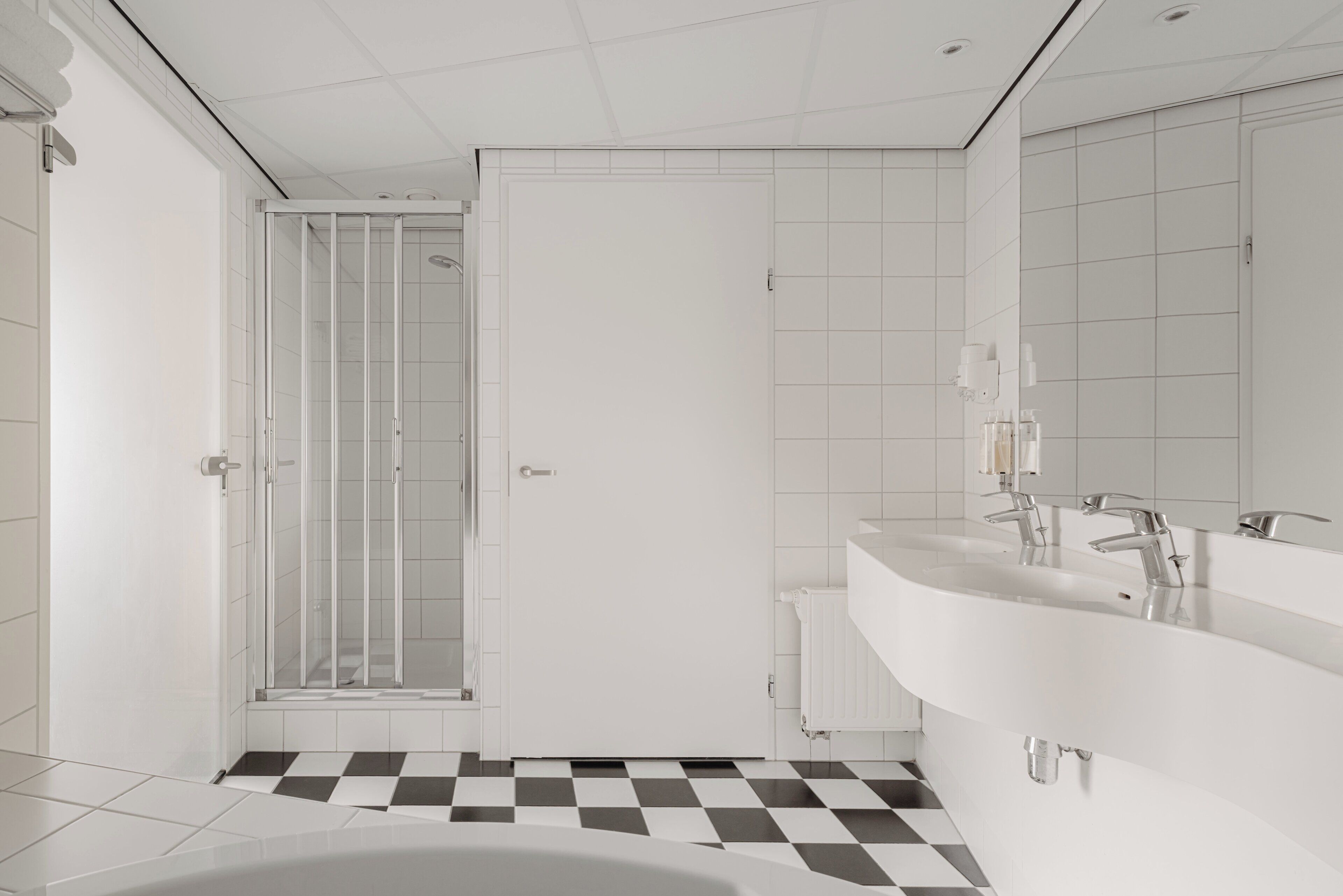 Et moderne badeværelse med skakmønstret gulv, brusekabine i glas og dobbelt vaskeskab.