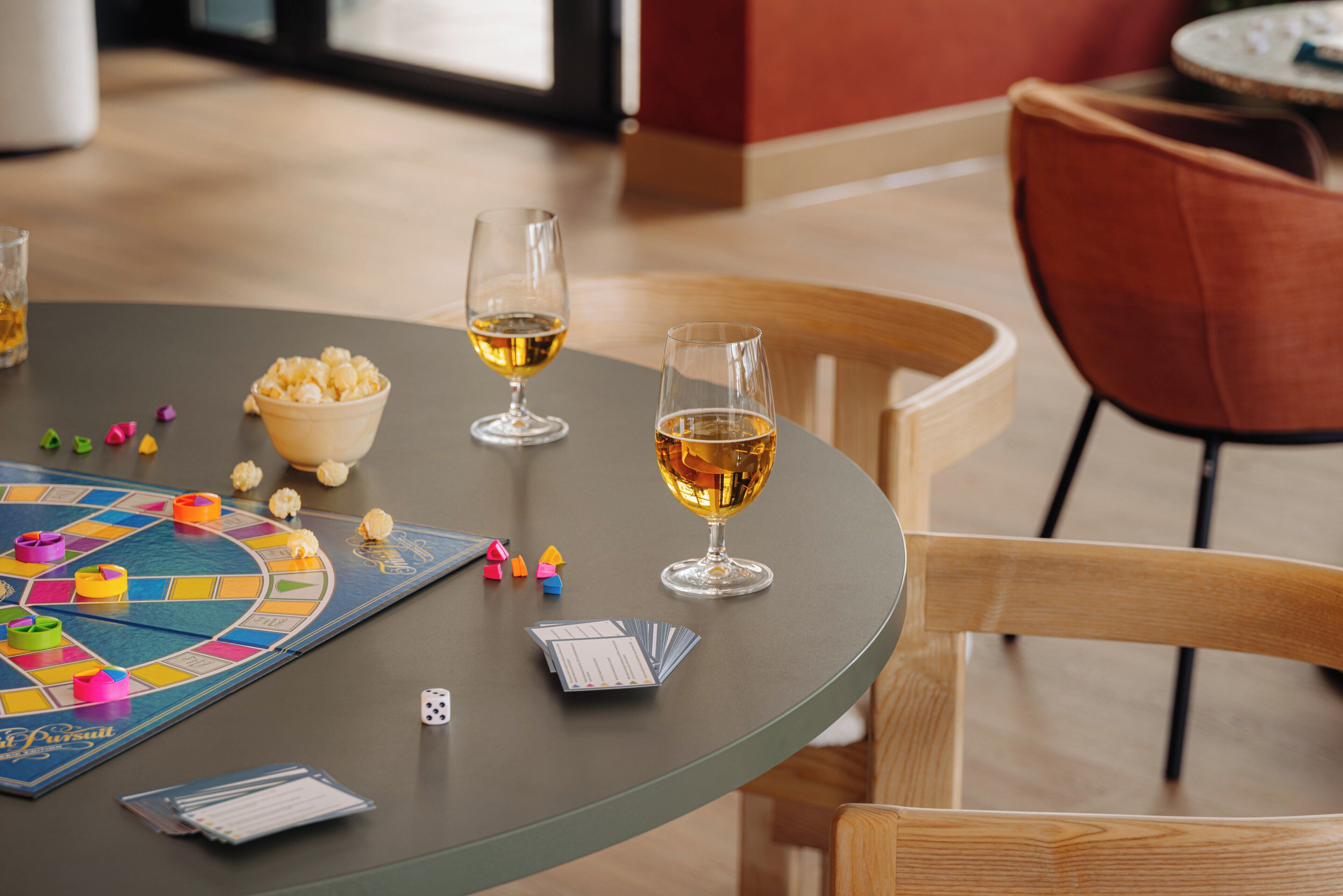 Una mesa con un juego de mesa, dos copas de vino, un bol de palomitas y cartas.