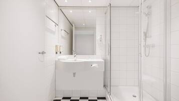 A modern bathroom with a glass shower enclosure, a white sink, and a checkered floor.