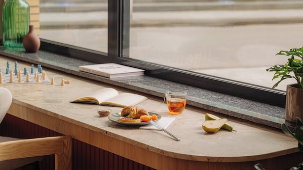A breakfast table with a chessboard, a book, a croissant, a plate with fruit, and a glass of tea. - Leonardo Hotel Hengelo City Center (Hengelo)