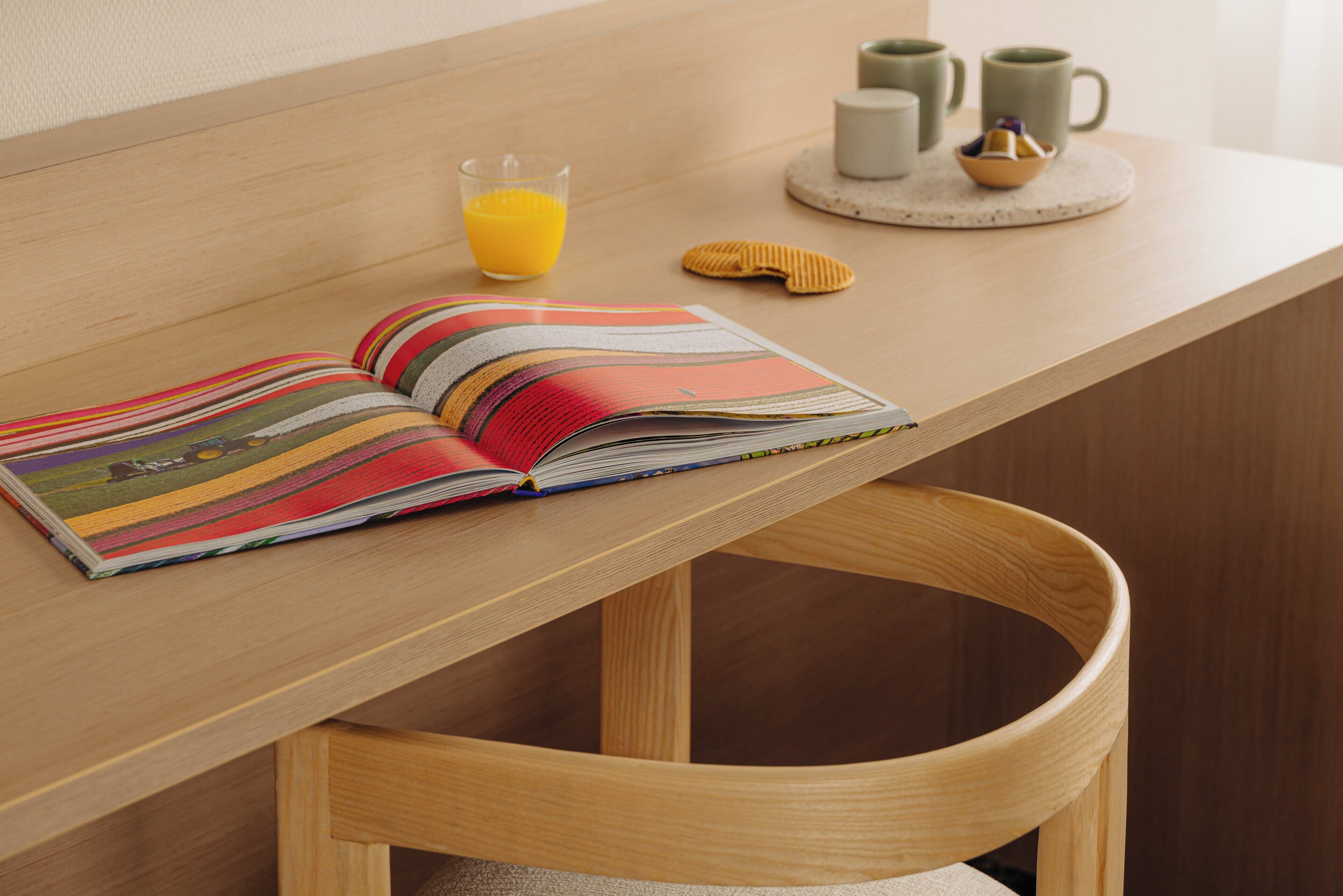 Una mesa de madera con un libro, un vaso de zumo de naranja y un bol pequeño.