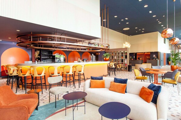 Relax in our inviting lobby, featuring a central bar, comfortable seating, and lush greenery.