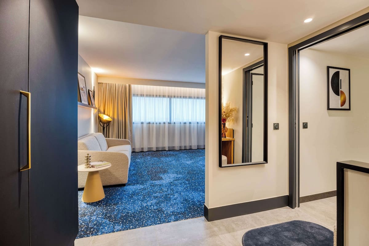 Une chambre d’hôtel moderne avec un tapis bleu à motifs, un canapé, une petite table ronde et un grand miroir.