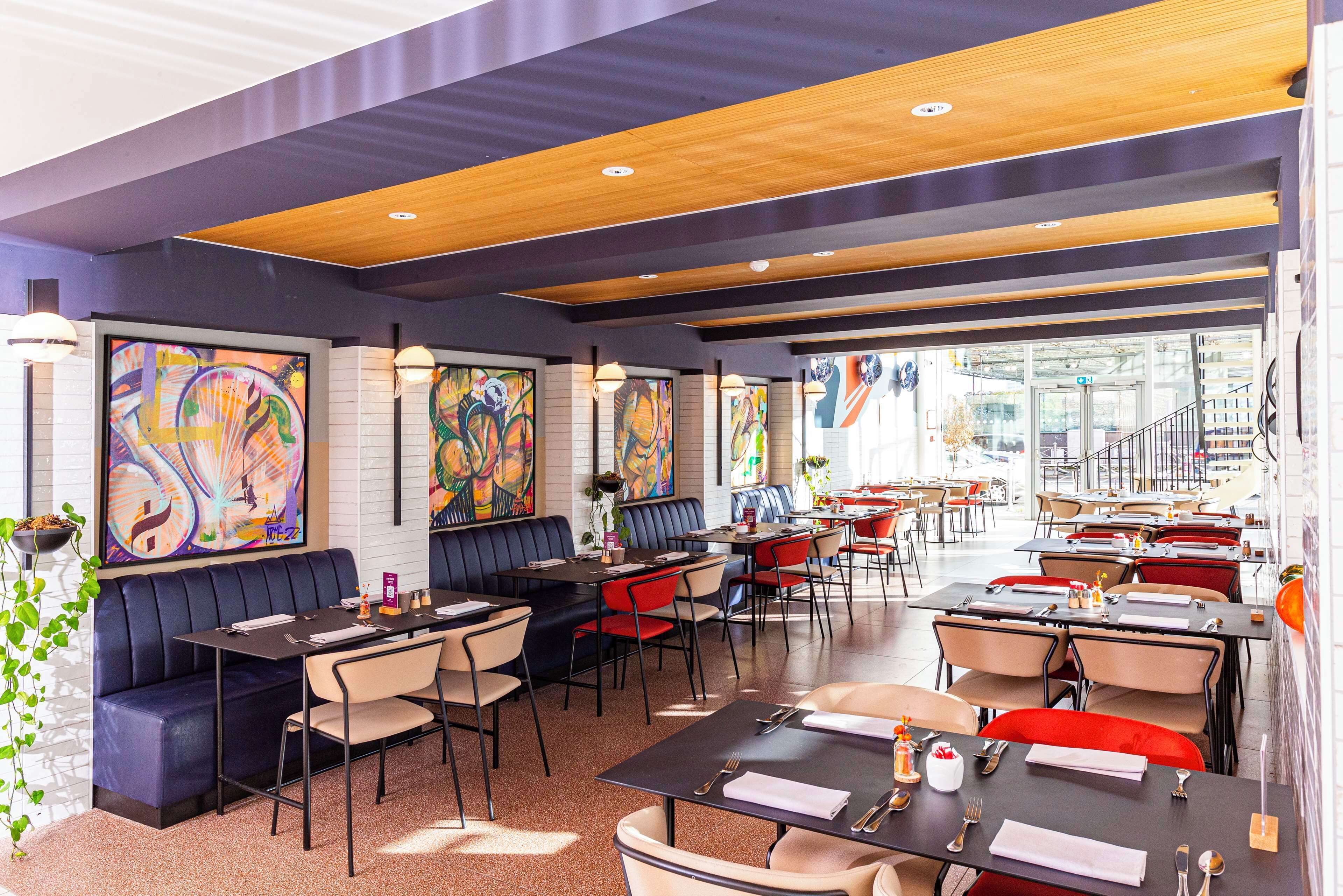 Un restaurante moderno con cabinas y mesas, grandes cuadros abstractos en las paredes y una escalera que conduce a un nivel superior.