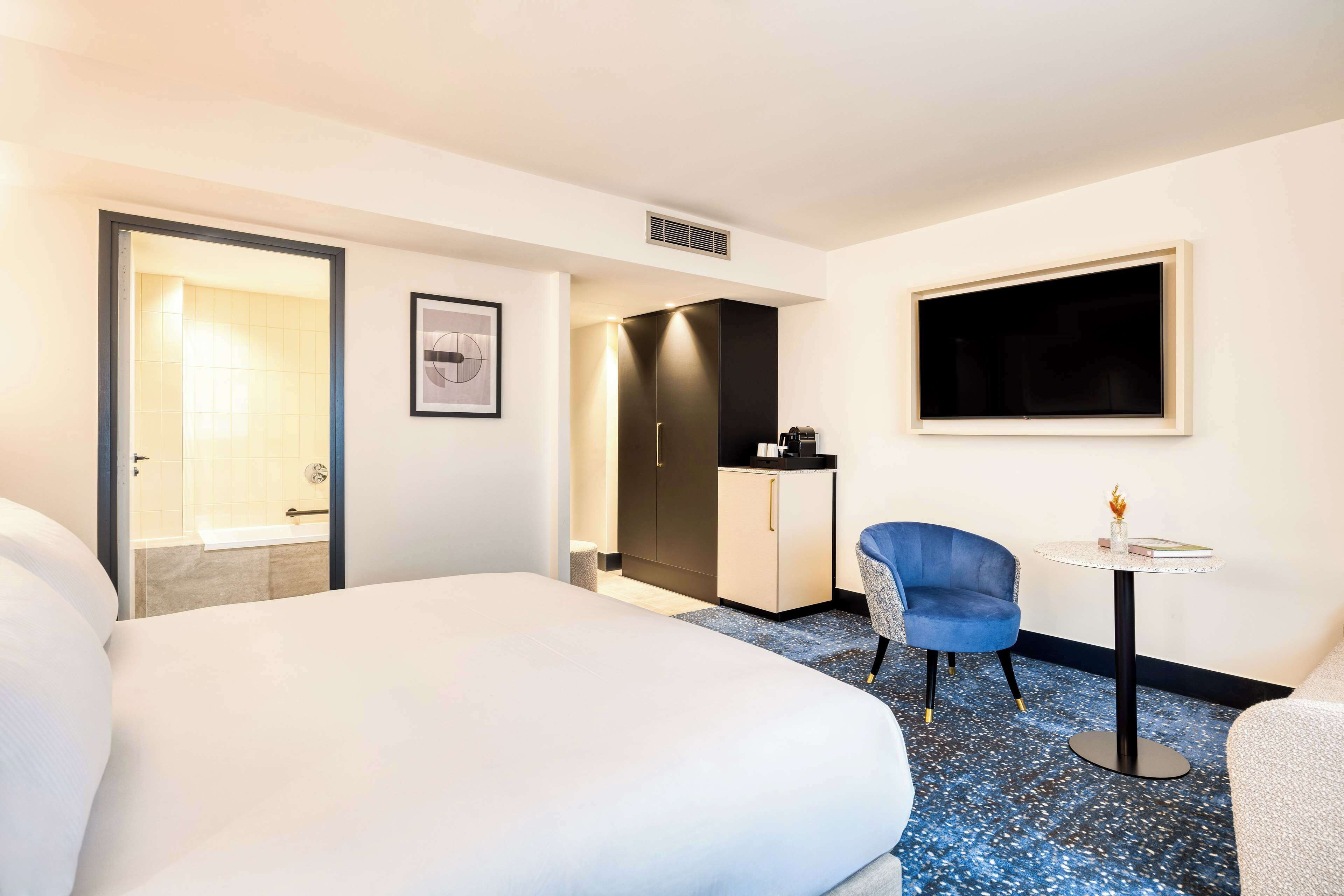 A hotel room with a large bed, a small desk, a chair, and a TV on the wall.