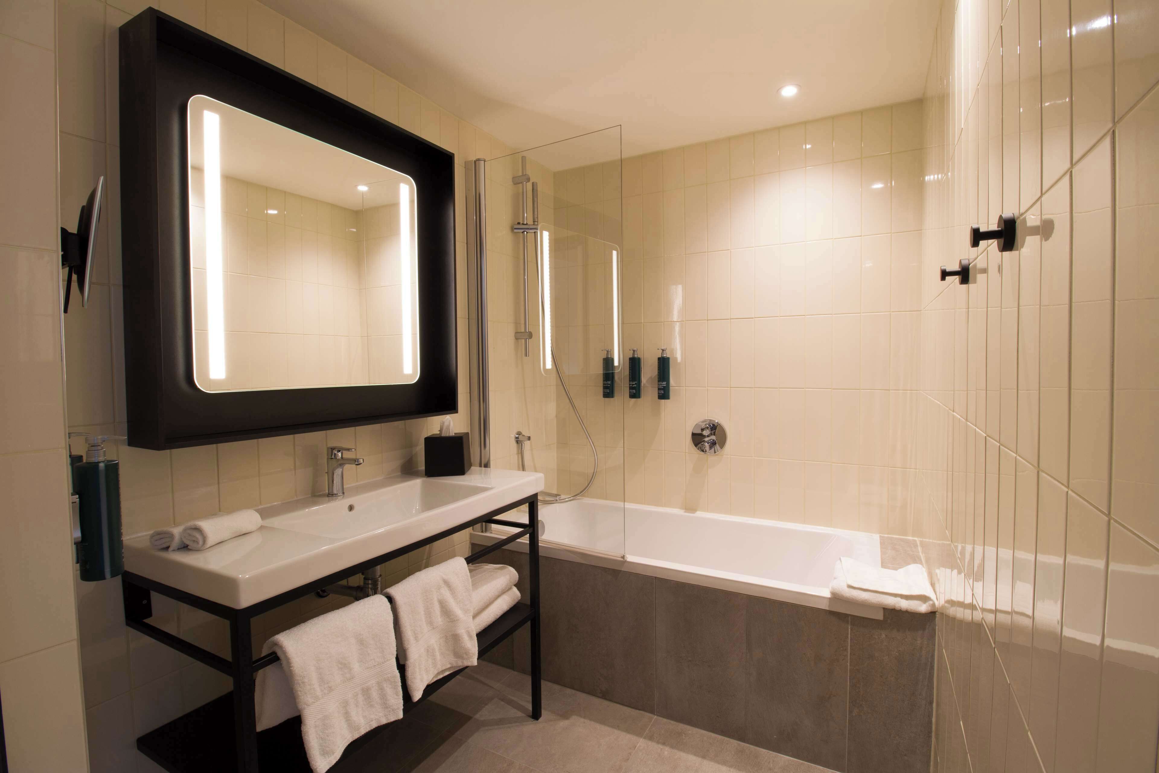 A modern bathroom with a large mirror, a sink, a bathtub, and a shower.