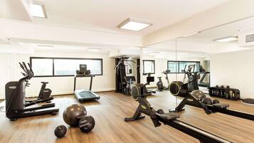 A gym with cardio machines, free weights, and a mirrored wall.