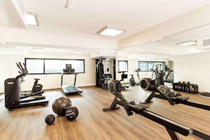 Un gimnasio con máquinas de cardio, pesas libres y un espejo grande.