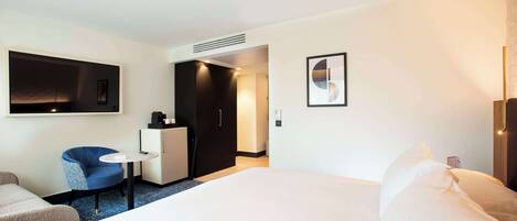 A hotel room with a large bed, a small round table, a blue chair, a desk, and a wardrobe.