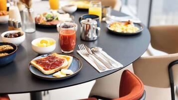 A breakfast table with various dishes, including toast with jam, a bowl of fruit, and a glass of orange juice.
