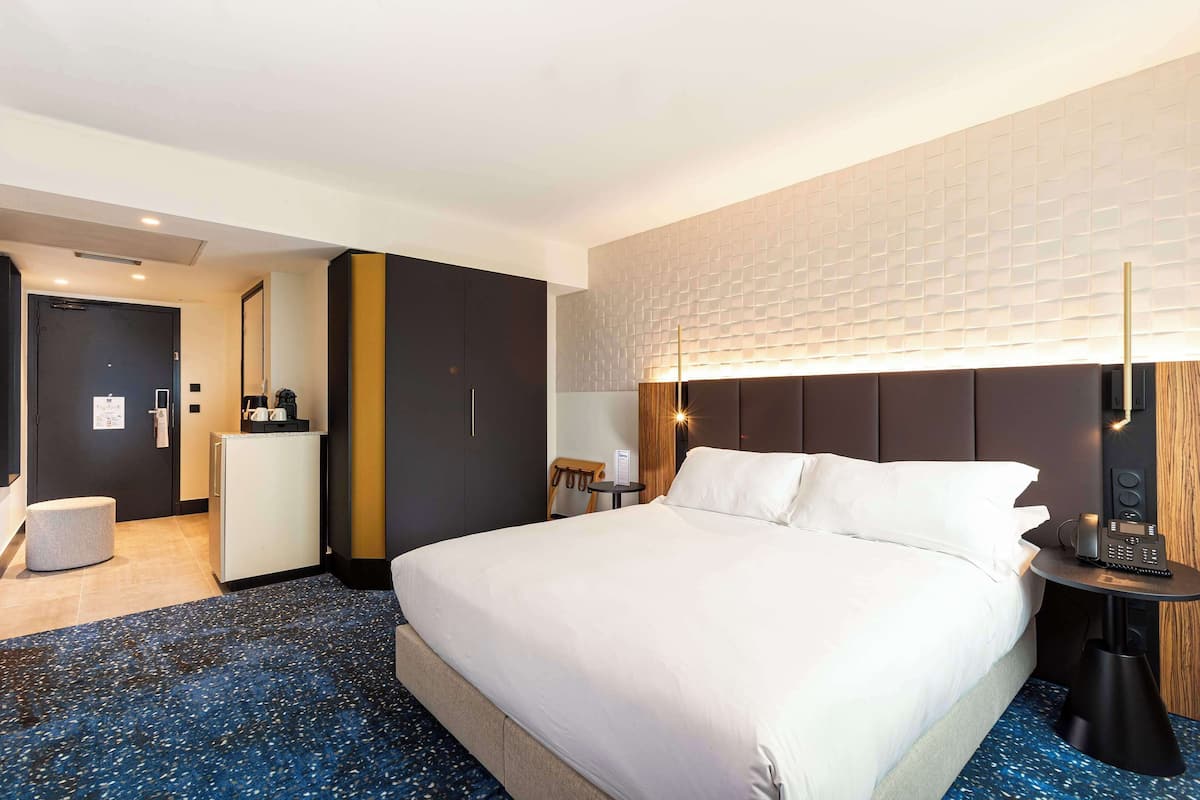 Une chambre d’hôtel avec un grand lit, un bureau, une chaise, une petite table, une lampe et un téléphone fixé au mur.