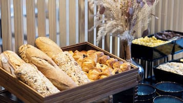 Una bandeja de madera exhibe panes y pasteles variados, con plantas secas decorativas al fondo.