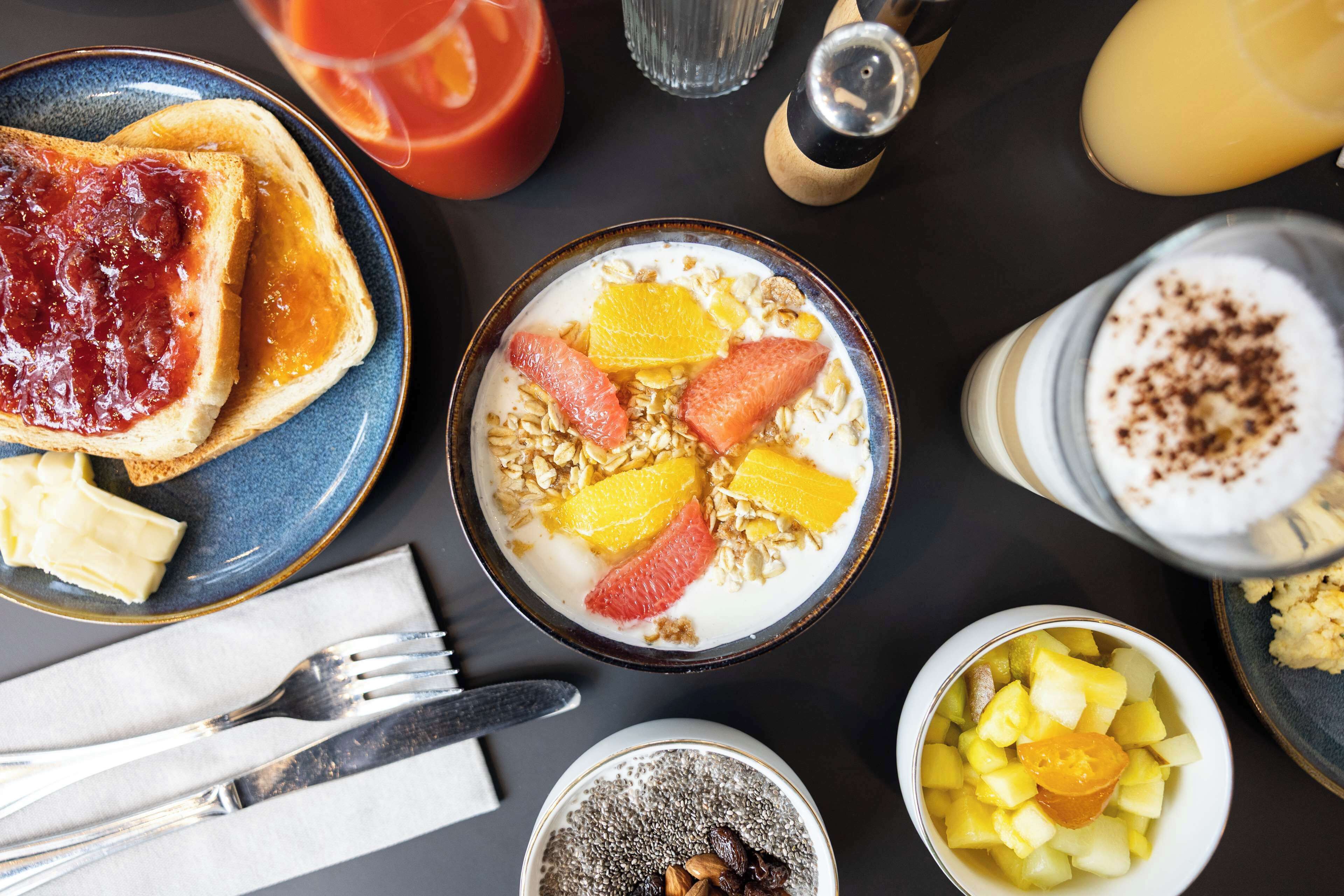 A breakfast setting with toast, cereal, fruit, and a glass of orange juice.