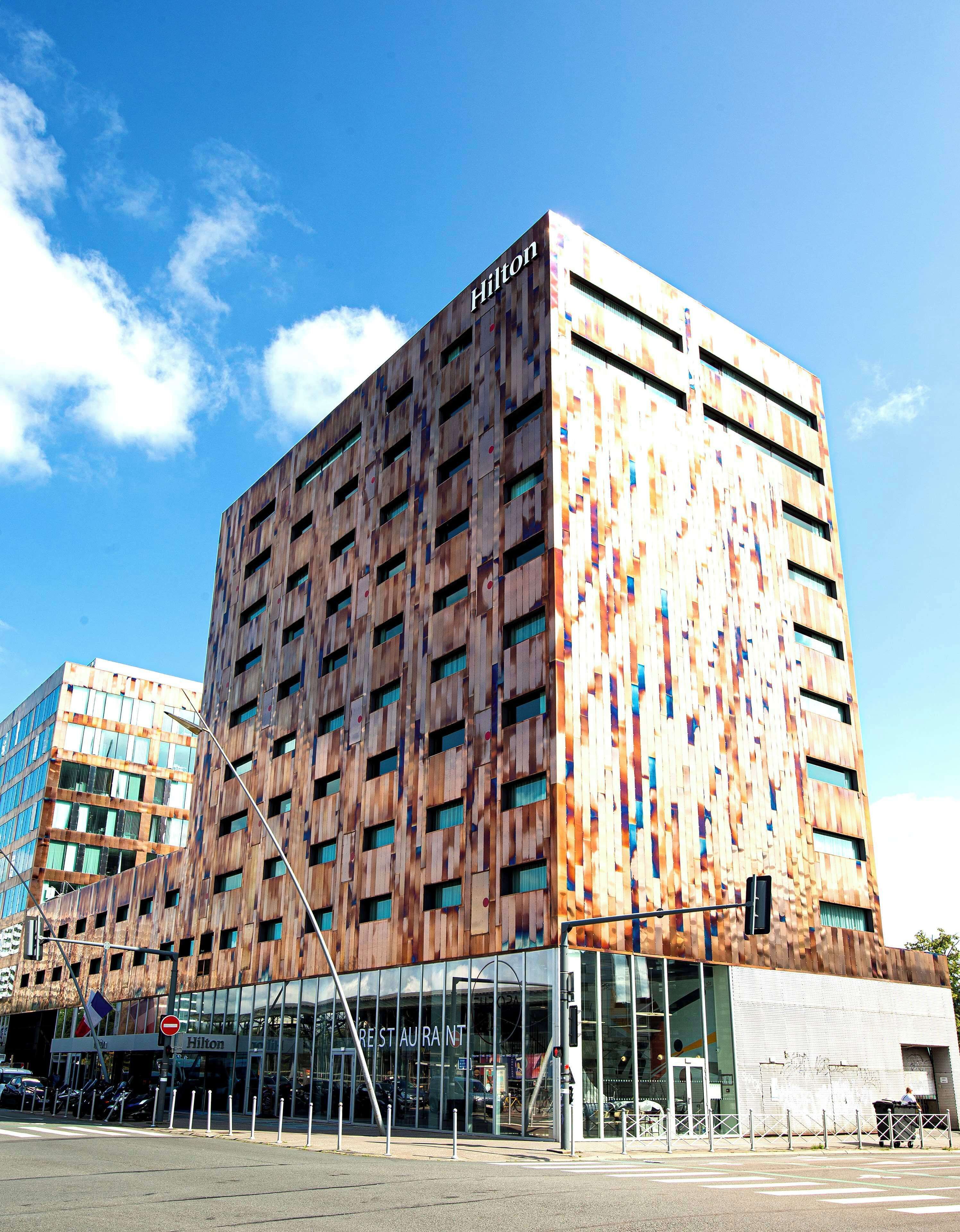 Un edificio moderno con el letrero 'Hilton', que presenta una fachada de madera única y amplios ventanales.