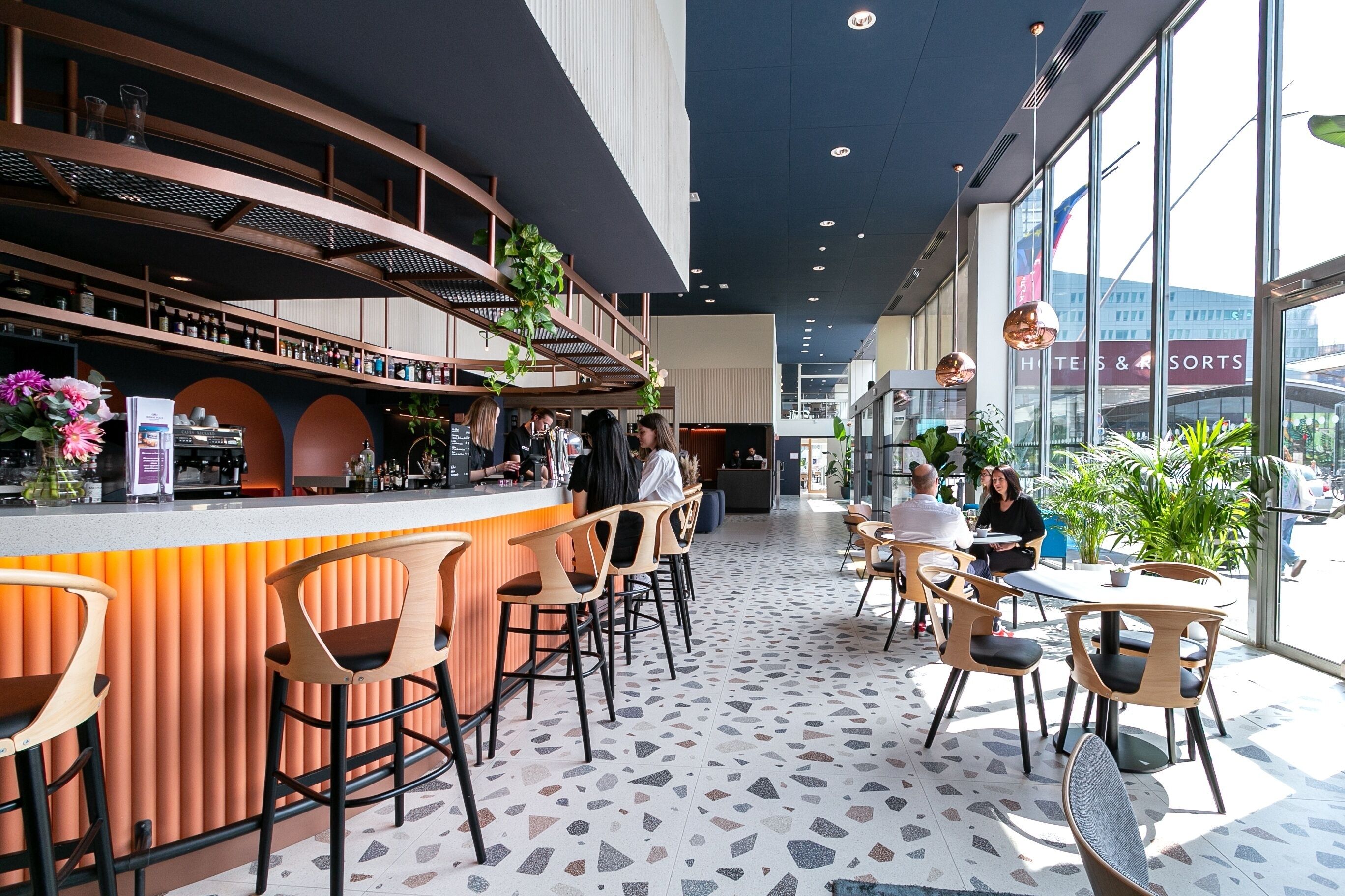 Un espace bar moderne doté d’un comptoir incurvé, de tabourets de bar et d’une variété d’aménagements, notamment des tables et des chaises rondes.