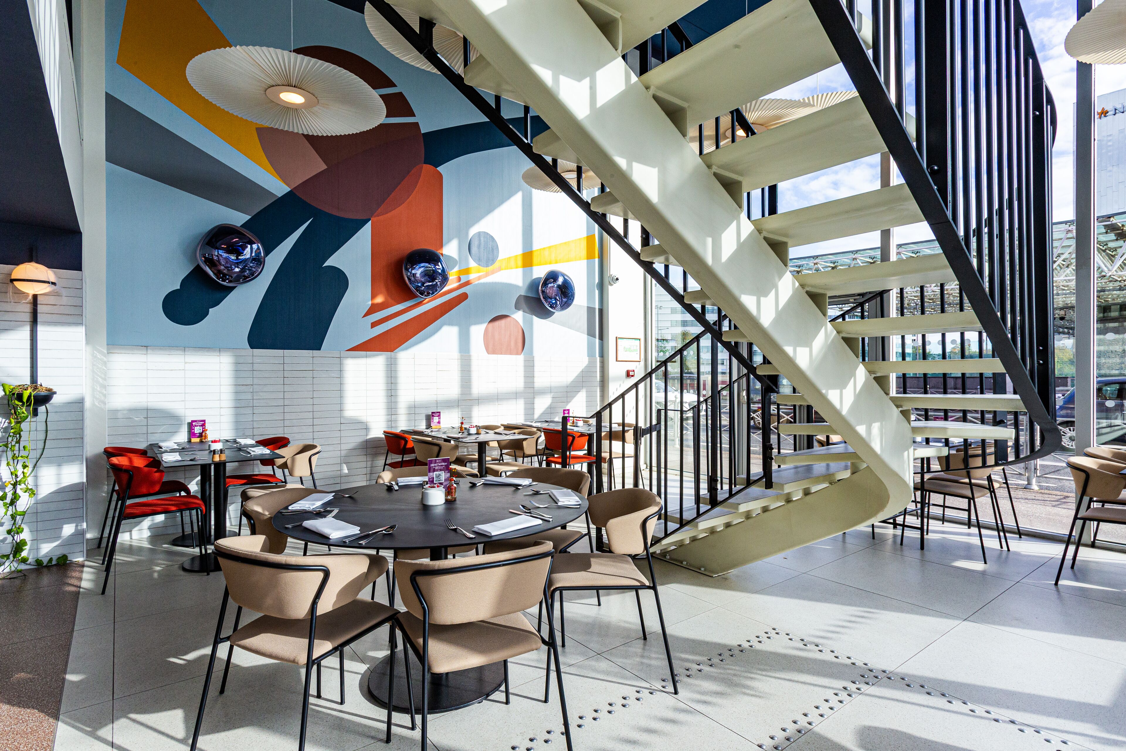 A modern interior with a spiral staircase, round tables, and chairs arranged around a central area.