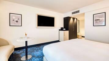 A hotel room with a bed, a small round table with a vase, a TV, a wardrobe, and a framed picture on the wall.