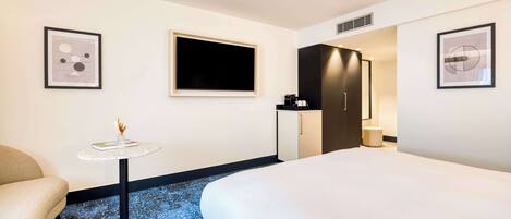 A hotel room with a bed, a small round table with a vase, a TV, a wardrobe, and a framed picture on the wall.