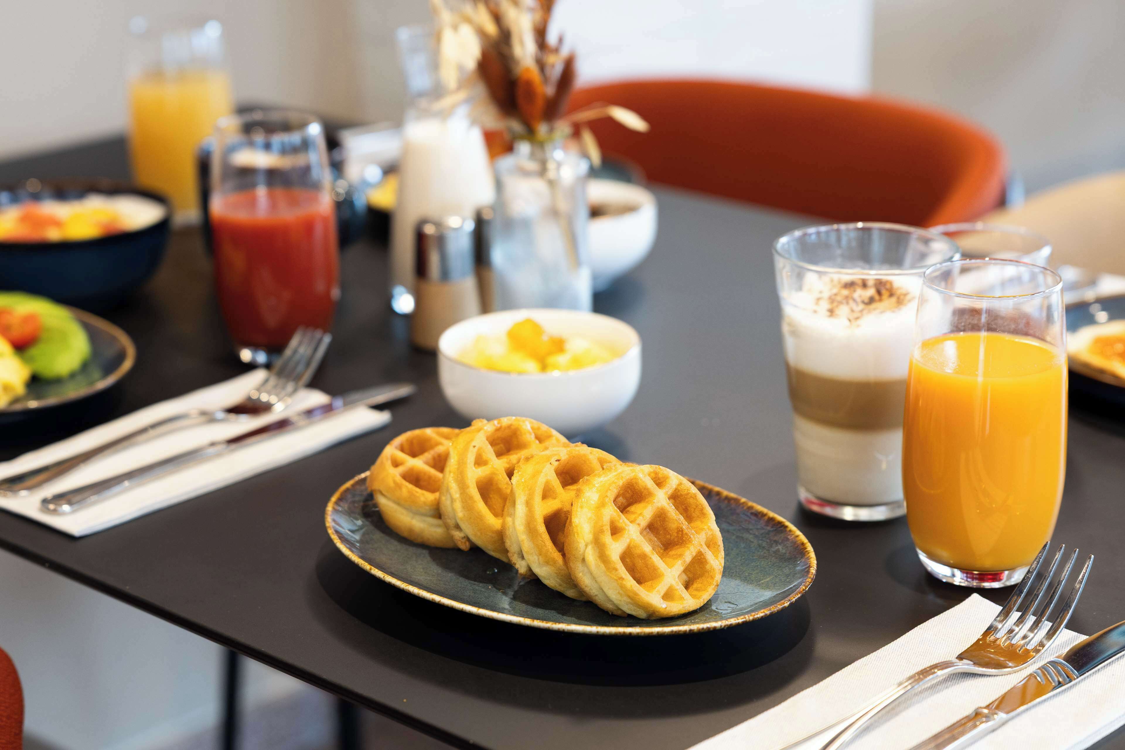 A breakfast setting with waffles, orange juice, and a bowl of fruit.