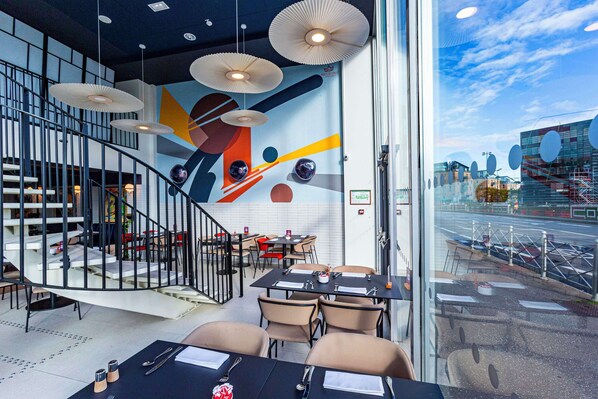 Un restaurante moderno con una escalera espiral, muebles contemporáneos y un mural colorido.