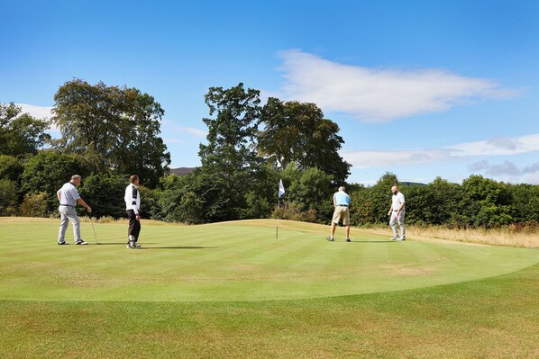Un campo de golf con tres jugadores, árboles y cielo despejado.