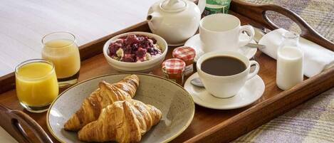 Un plateau de petit-déjeuner avec des croissants, du jus, du café et un bol de fruits rouges.