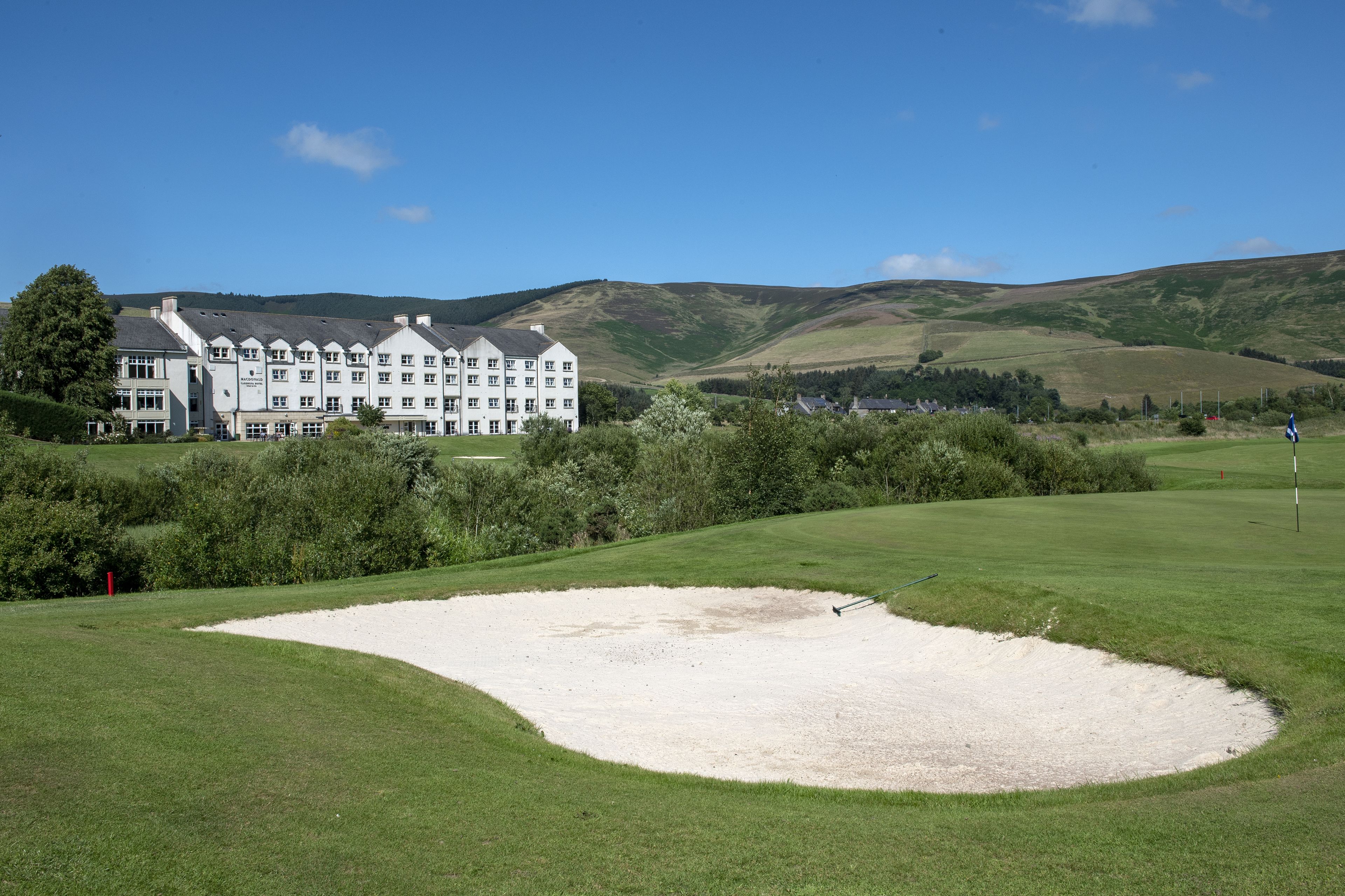 A golf course with a sand bunker and a large white building in the background.