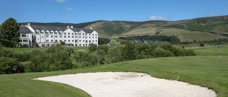 A golf course with a sand bunker and a large white building in the background.