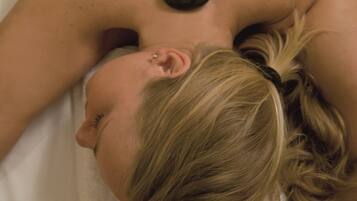 A person receiving a back massage with stones placed along the spine.