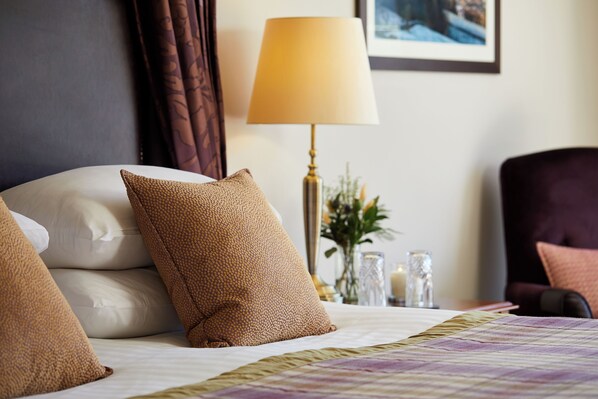 A neatly made bed with multiple pillows, a bedside lamp, and a vase with flowers.